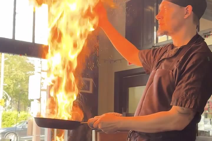 A chef tilts a flaming pan during the food tour, flame rising tall above the pan
